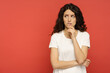 Serious doubtful italian woman looking up thinking pensive and confused. Young curly girl in white outfit isolated on red background. Concerned upset female in 30s bite lips in doubts and thoughts