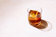 Whiskey or bourbon in a rocks glass with a big ice cube, shot with hard light and harsh shadows, bright backdrop, copy space
