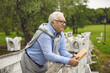 © Studio Romantic - Pensive senior man holding book standing on bridge in park thinking looking forward enjoy rest and relax outdoors. Elderly retired male grandparent in romantic mood remember best vibes