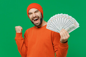 Wall Mural - Young happy caucasian man 20s wear orange sweatshirt hat holding fan of cash money in dollar banknotes do winner gesture isolated on plain green background studio portrait. People lifestyle concept.