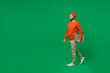 Full body young smiling happy caucasian man 20s wear orange sweatshirt hat hold closed laptop pc computer walking going isolated on plain green background studio portrait. People lifestyle concept