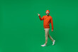 Full body young smiling happy cheerful surprised man 20s wear orange sweatshirt hat goign walking strolling point index finger aside on workspace isolated on plain green background studio portrait