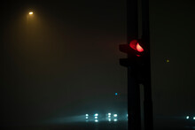 Closeup view of semaphore, red light and foggy night atmosphere. Car lights and traffic in background. Night scene.