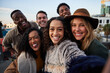 © StratfordProductions - Multi-cultural group of friends taking a selfie at a rooftop party. Smiling and posing at camera in the city.