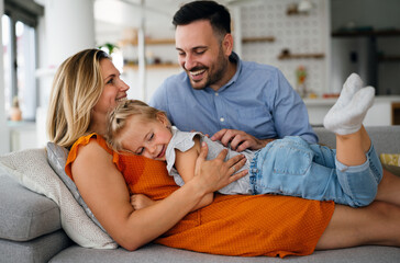 Wall Mural - Parents having fun with their little daughter on bed. Family spending time at the morning.