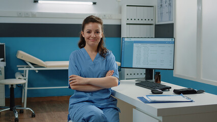 Wall Mural - Portrait of medical assistant standing with arms crossed in cabinet for medical checkup visit. Woman nurse working with computer and documents in doctors office for healthcare system.