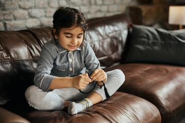 Wall Mural - Smiling Muslim girl holds prayer beads while sitting on  sofa at home.