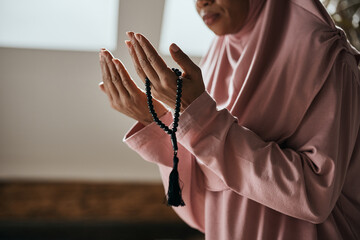 Wall Mural - Close up of black Muslim woman uses prayer beads while praying at home.