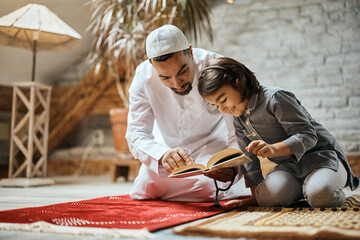 Wall Mural - Happy Muslim girl and her father read Koran at home.