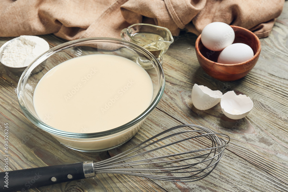 Raw batter with whisk and ingredients on wooden background