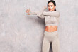 © halayalex - Fitness confident woman in sports clothing. Sexy young beautiful model with perfect body. Female posing near grey wall in studio. Stretching out before training