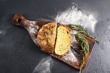 Wall Mural - a sliced round loaf of mustard bread with rosemary on a wooden board and a black background. top view.