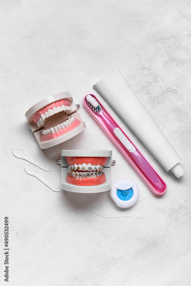 Model of jaws with braces, toothbrush, dental floss and paste on light background