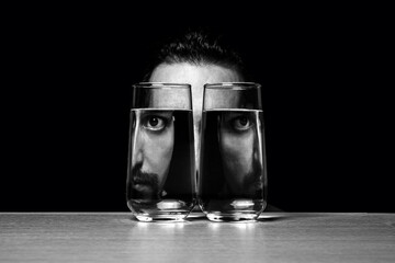 A man looks through two glasses of water on a black background. Distortion through the water. creative portrait