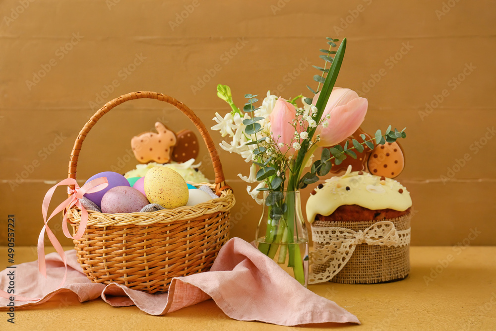 Gift basket with painted Easter eggs, flowers and cake on table