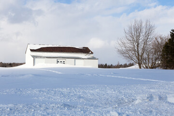 Wall Mural - Large white barn in pristine snowy field against light white clouds and blue sky seen during a winter afternoon, Quebec City, Quebec, Canada