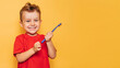 The happy kid is holding a blue toothbrush on a yellow background and smiling showing his teeth. Health care, oral hygiene. A place for your text.