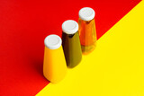 Fototapeta Młodzieżowe - Bottles with yellow and red liquid halthy beverage on yellow and red background. Orange apple cherry