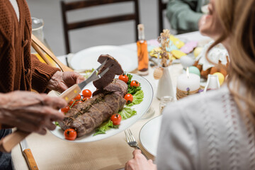 cropped view of senior woman serving meat near adult daughter during easter dinner.