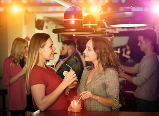 Wall Mural - Portrait of smiling young women drinking cocktails and talking on party