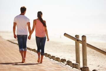 enjoying a walk down memory lane. rear view shot of a young couple walking along the beach holding h