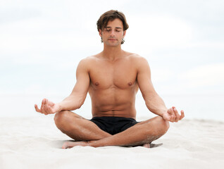 Wall Mural - Be still and listen to what nature has to say. Young handsome man sitting on the beach meditating.