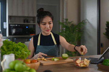 Wall Mural - Young vegetarian woman preparing healthy salad in kitchen. Healthy lifestyle concept.