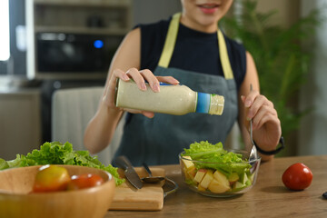 Wall Mural - Young housewife pouring sauce  from bottle into vegetable salad.