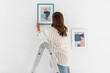 home improvement, decoration and people concept - woman on ladder hanging picture in frame on wall