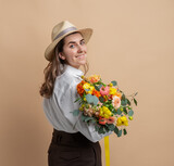 Fototapeta Tulipany - people, portrait and floral design concept - happy smiling woman in straw hat holding bunch of flowers over beige background