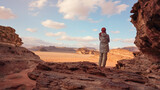 Fototapeta  - Young woman standing on rocky ground in desert landscape, view from behind. Wadi Rum, Jordan