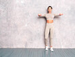 © halayalex - Fitness confident woman in sports clothing. Sexy young beautiful model with perfect body. Female posing near grey wall in studio. Stretching out before training.Making exercises with dumbbells