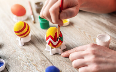 Wall Mural - Woman's hand with a brush is drawing a colored pattern on an Easter egg. Preparation for the bright Easter holiday