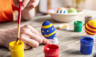 Wall Mural - Woman's hand with a brush is drawing a colored pattern on an Easter egg. Creative preparation for bright Easter holiday