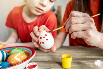 Wall Mural - Woman's hand with a brush is drawing a colored pattern on an Easter egg. Creative preparation for bright Easter holiday