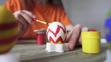 Wall Mural - Hand with a brush is drawing a colored pattern on an Easter egg. Creative preparation for bright Easter holiday