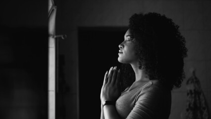 A woman praying at home by window having HOPE and FAITH in monochrome