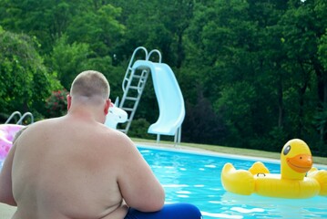 father watching children play in a backyard swimming pool