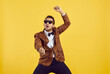 © Studio Romantic - Happy funny positive young black man dancing gangnam style isolated on a yellow colour background. Studio shot of a handsome goofy African guy in a leopard party jacket dancing to k pop music
