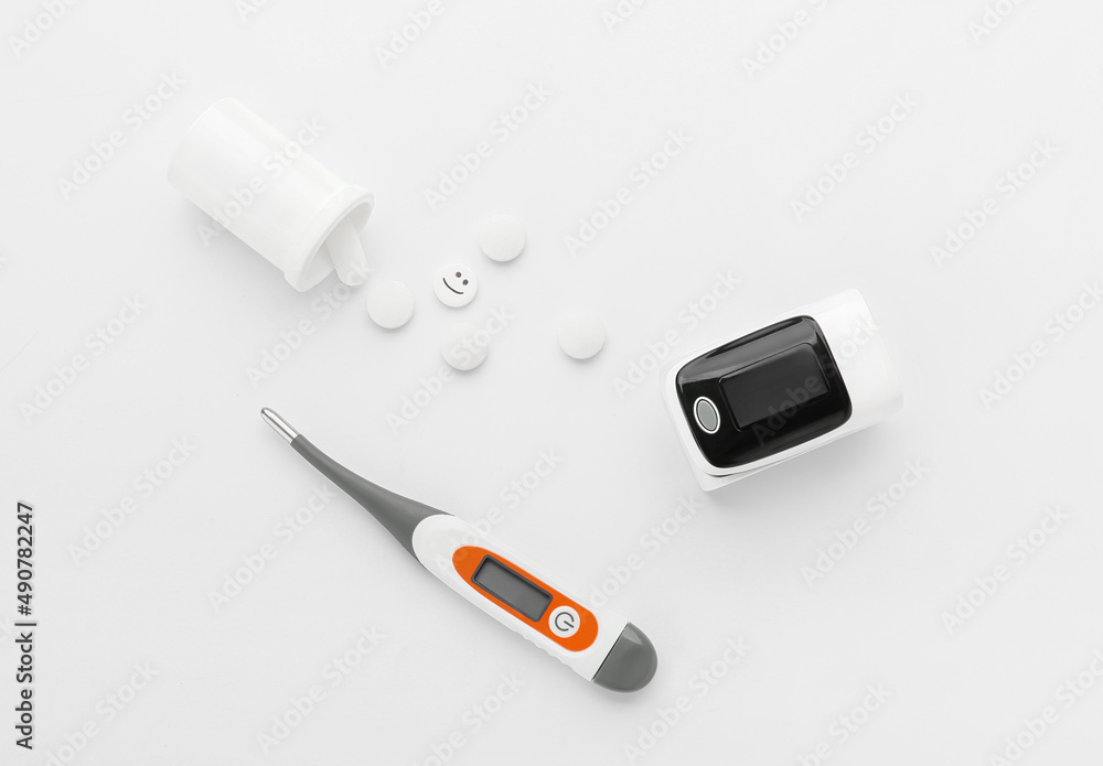 Pulse oximeter, thermometer and pills on white background
