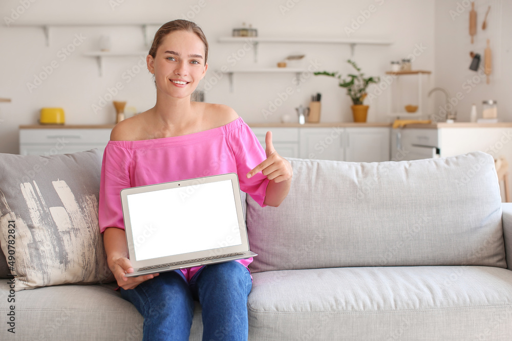 Young woman pointing at laptop with blank screen on sofa at home