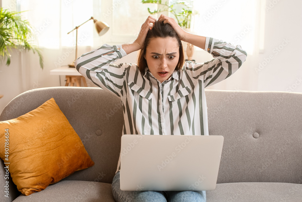 Emotional woman using laptop on sofa in light room. E-mail concept