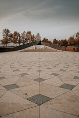 Wall Mural - Vertical photo of a square in a city with a monument, trees and a cloudy sky