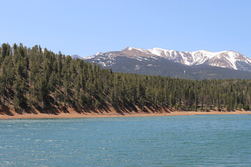 Wall Mural - Scenic view of a mountain forest by a lake with alpine mountain on background