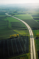 Poster - Aerial shot of a road surrounded by a green field on a sunny day