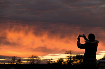 Wall Mural - Woman taking a photo of the beautiful sunset with a cloudy sky