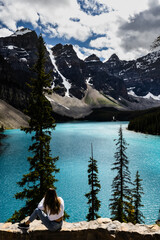 Canvas Print - Female sitting on a wall and facing the blue river in mountains