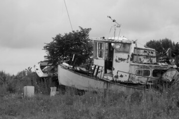 Black white photo of old boat washed ashore with sea and cloudy sky on the background