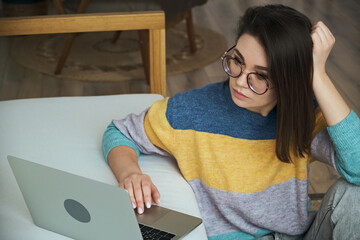 Wall Mural - Young woman using laptop, using touchpad sitting on the floor near the sofa at home, remote work, work at home