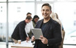 © Thurstan Hinrichsen/peopleimages.com - Technology adds so much ease into the workplace. Portrait of a young businessman using a digital tablet in an office with his colleagues in the background.